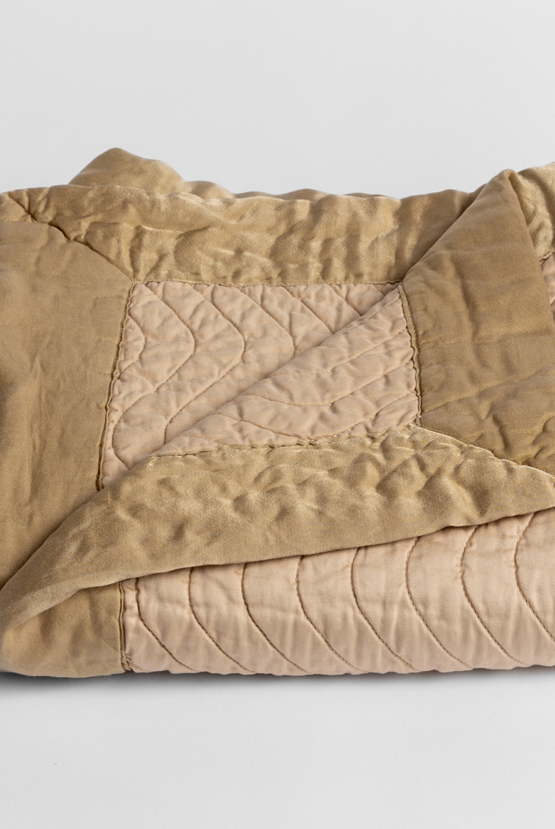 Honeycomb: a folded quilted cotton sateen baby blanket with its corner folded down to show the trim contrast - shot against a white background. 