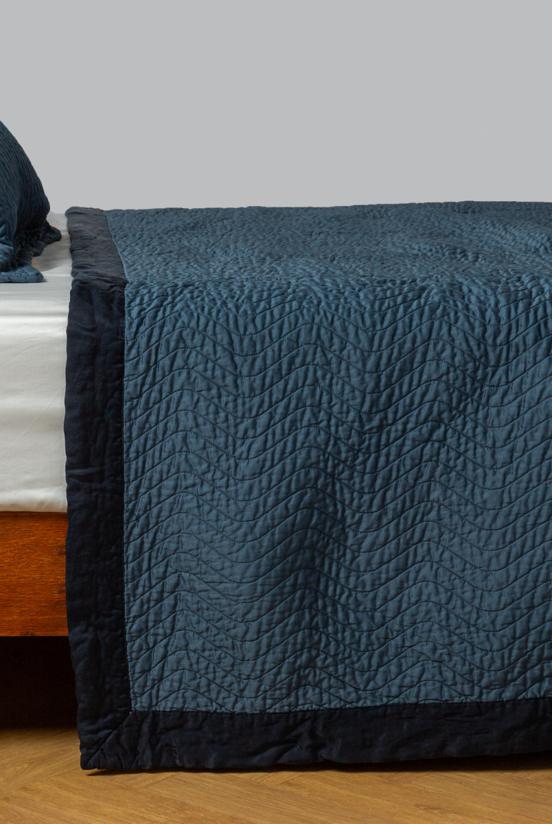 Midnight: quilted cotton sateen coverlet with matching sham on a winter white fitted sheet - side view. 