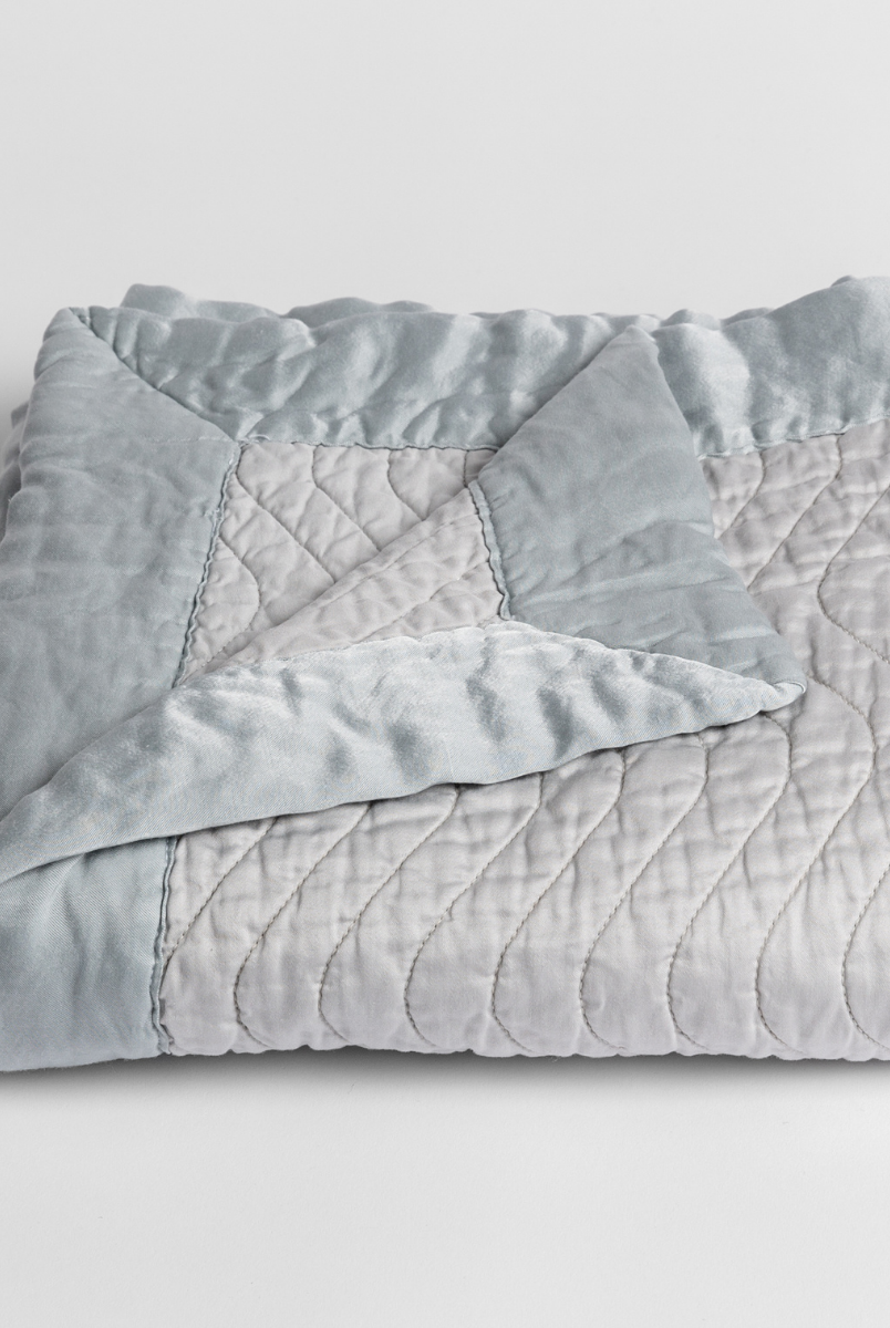 Cloud: a folded quilted cotton sateen baby blanket with its corner folded down to show the trim contrast - shot against a white background. 
