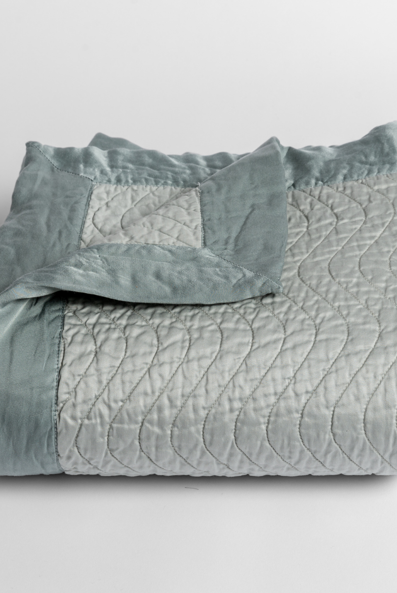 Eucalyptus: a folded quilted cotton sateen baby blanket with its corner folded down to show the trim contrast - shot against a white background. 