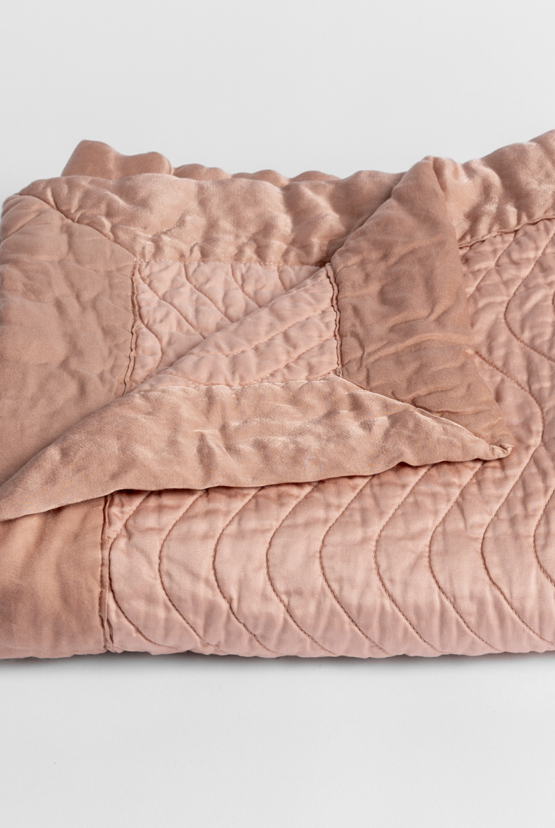 Rouge: a folded quilted cotton sateen baby blanket with its corner folded down to show the trim contrast - shot against a white background. 