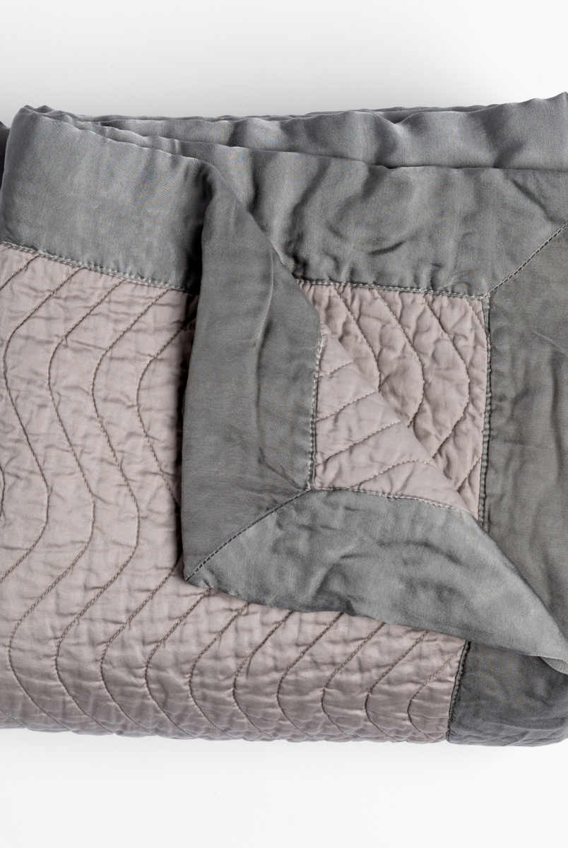 Fog: a folded quilted cotton sateen throw blanket with its corner folded down to show the trim contrast - shot against a white background. 