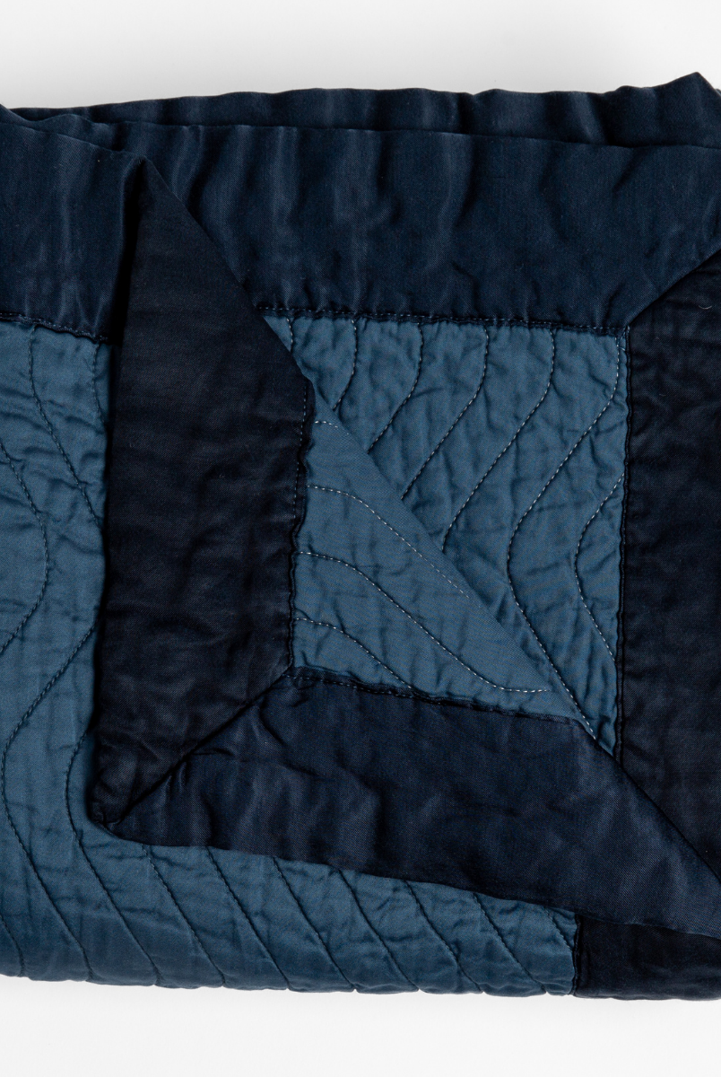 Midnight: a folded quilted cotton sateen throw blanket with its corner folded down to show the trim contrast - shot against a white background. 