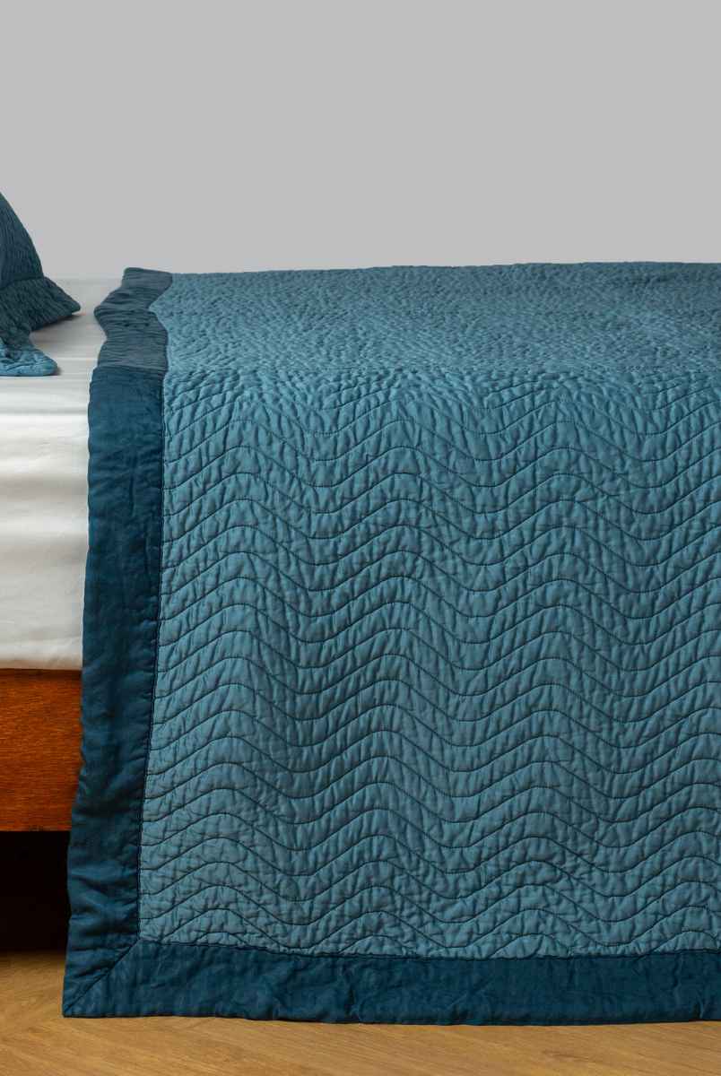 Cenote: quilted cotton sateen coverlet with matching sham on a winter white fitted sheet - side view. 