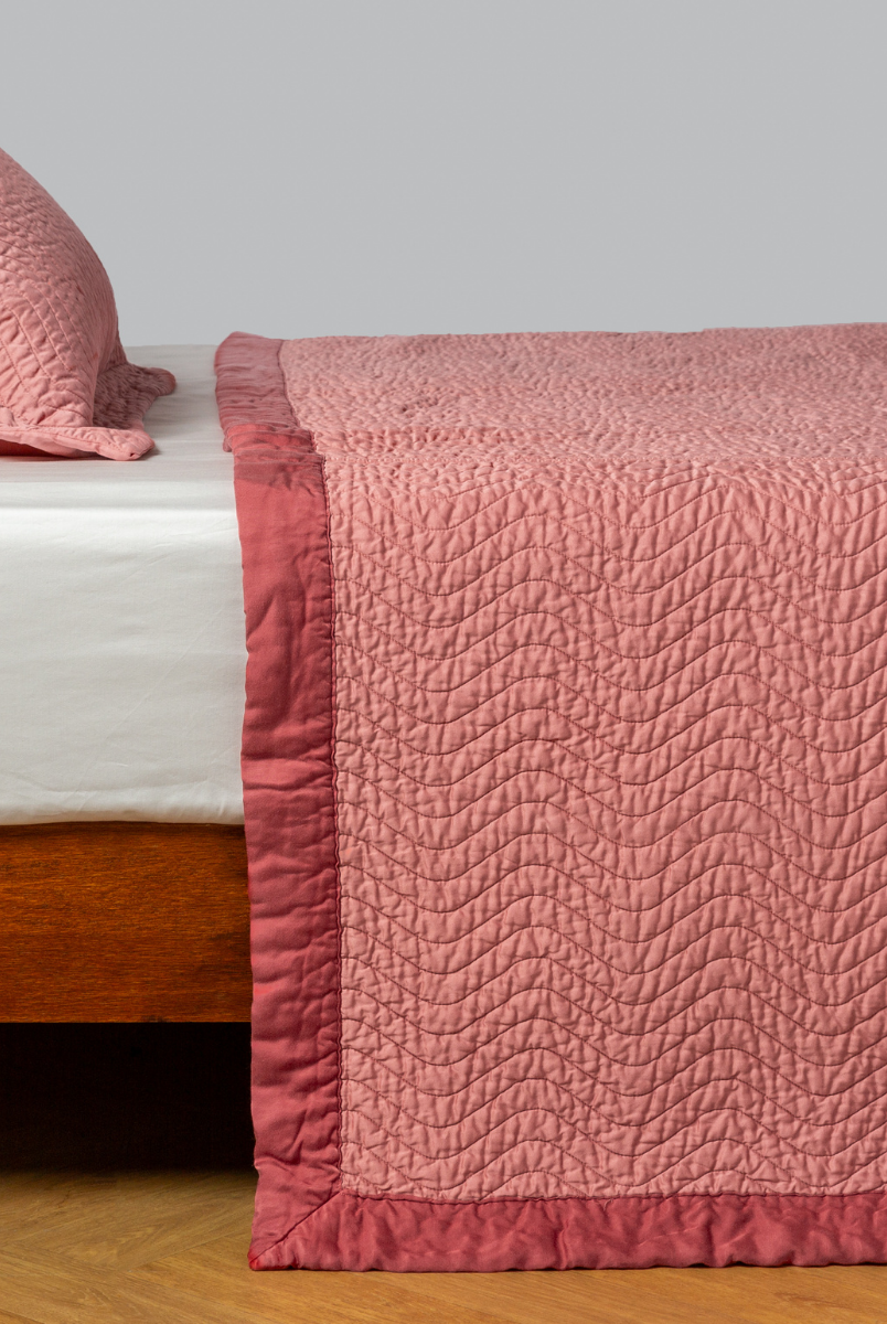 Poppy: quilted cotton sateen coverlet with matching sham on a winter white fitted sheet - side view. 