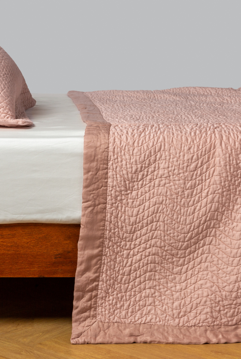 Rouge: quilted cotton sateen coverlet with matching sham on a winter white fitted sheet - side view. 
