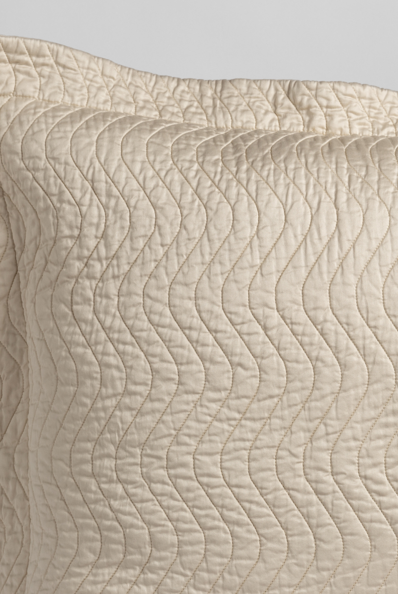 Parchment: a close up of a pillow corner showing the flange framing quilted cotton sateen shot against a white background. 