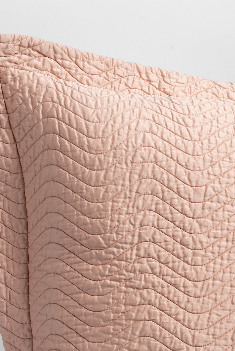 Rouge: a close up of a pillow corner showing the flange framing quilted cotton sateen shot against a white background. 
