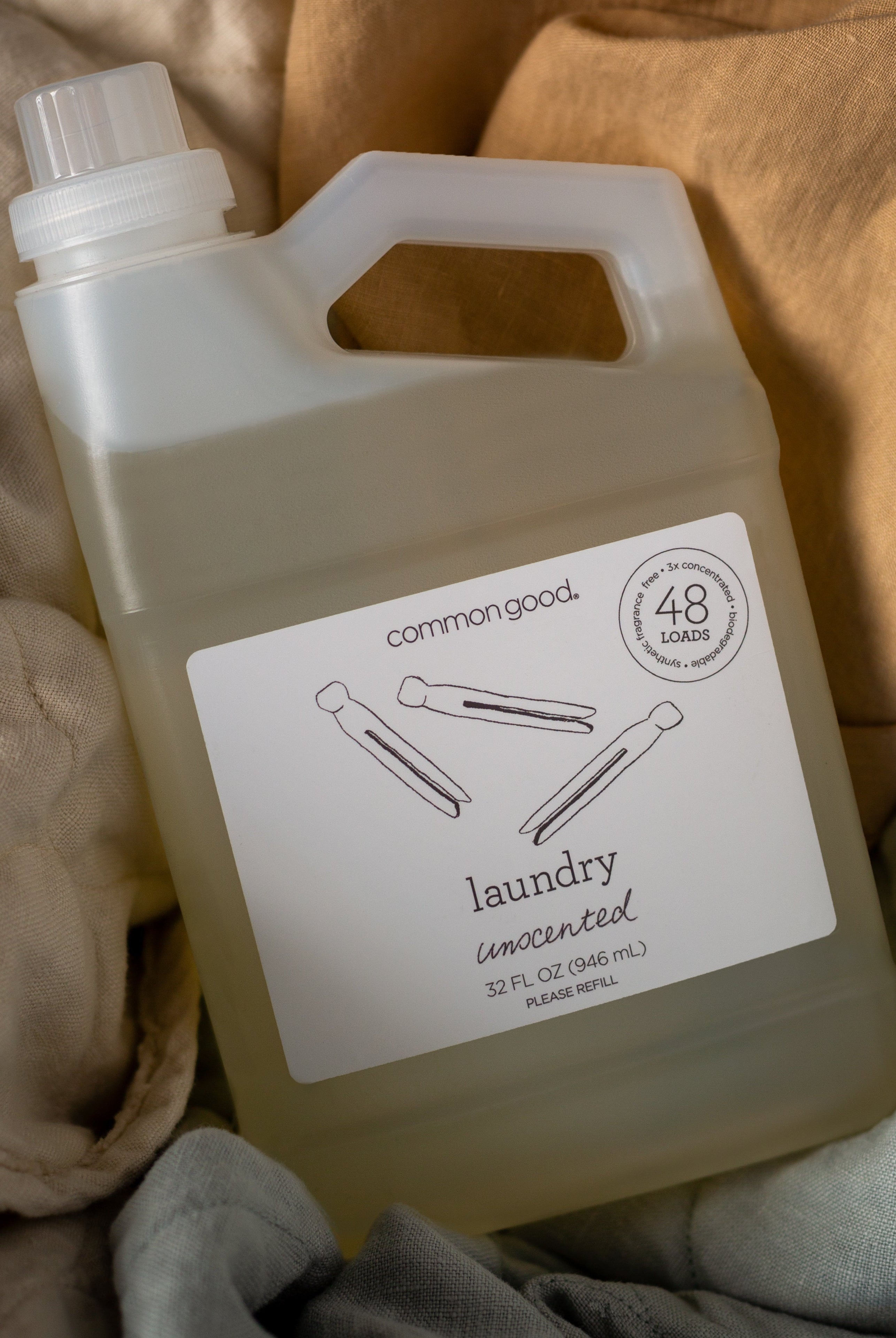 [allvariants]: a bottle of unscented common good laundry detergent shown from overhead  nested in linen fabrics in various colors. 